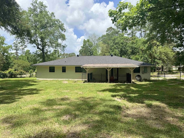 rear view of house featuring a lawn and fence