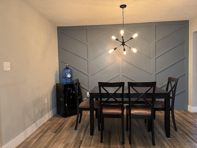 dining area featuring baseboards, wood finished floors, an inviting chandelier, and a decorative wall