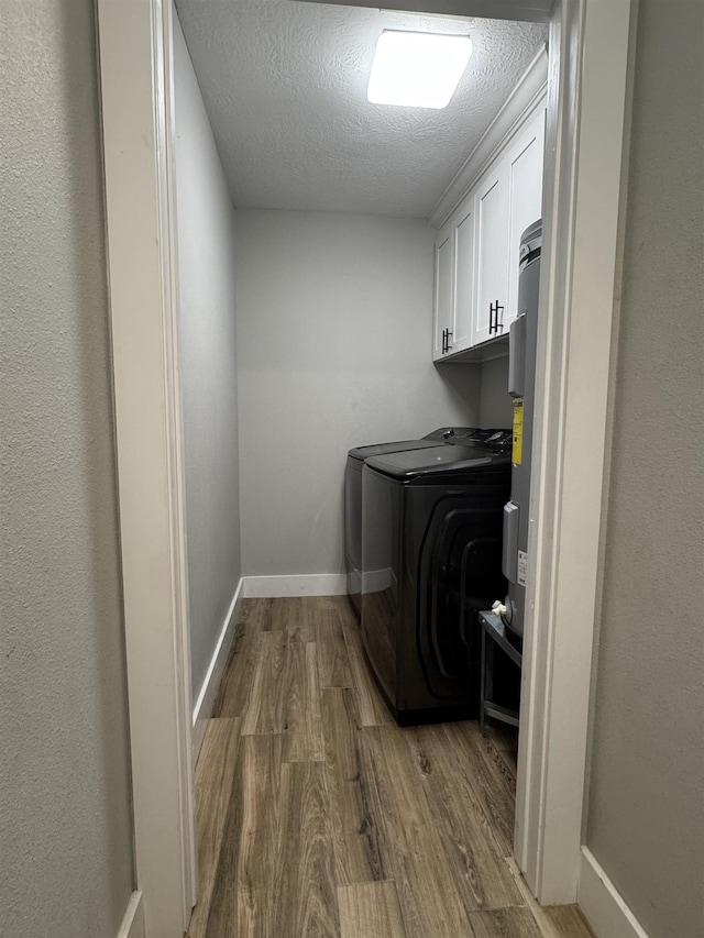 clothes washing area with wood finished floors, cabinet space, baseboards, washer / clothes dryer, and a textured ceiling
