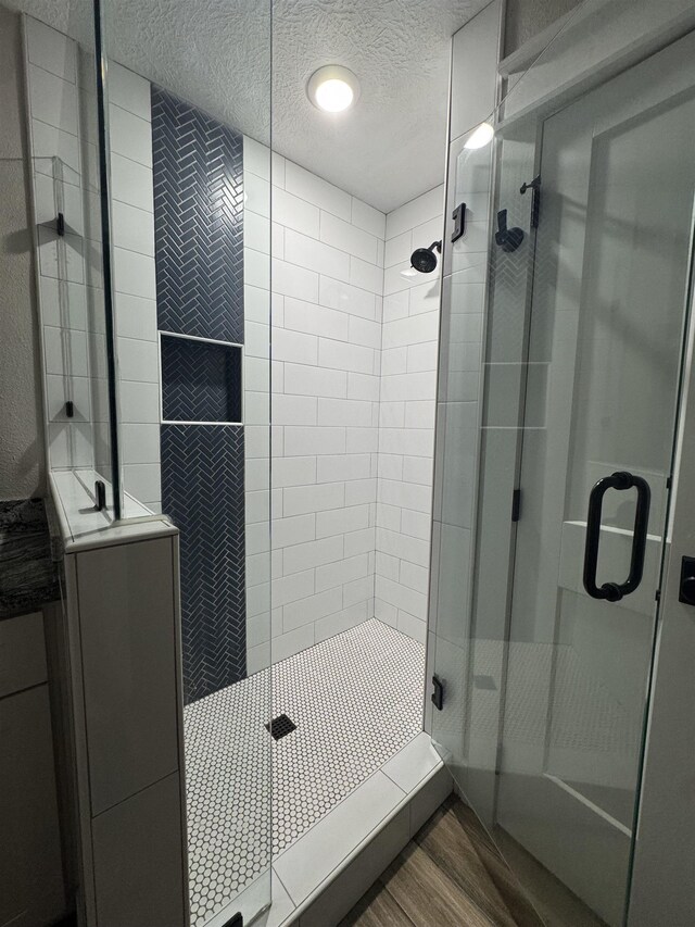 bathroom featuring a textured ceiling, wood finished floors, and a stall shower