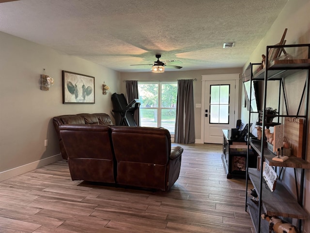 living area with a textured ceiling, ceiling fan, visible vents, and baseboards