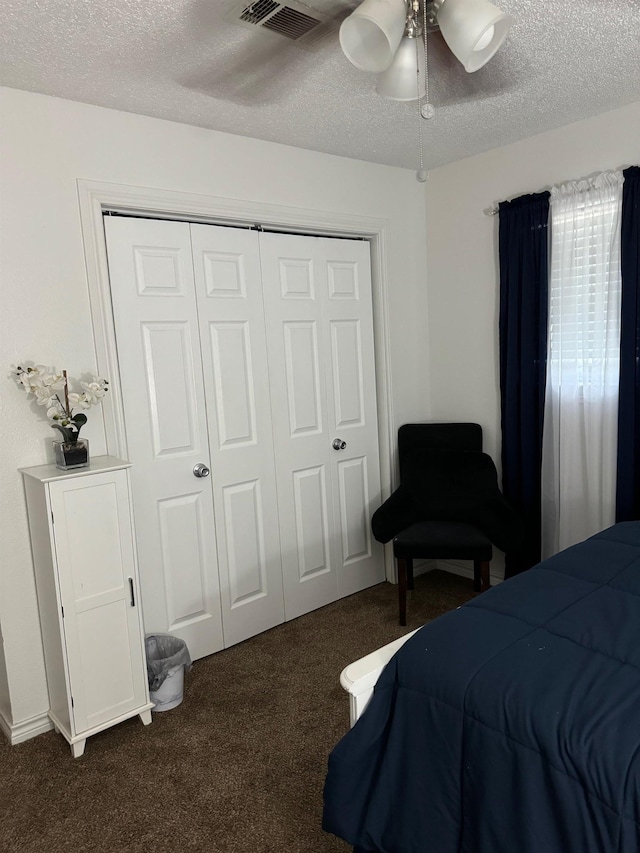 bedroom featuring a textured ceiling, a closet, dark carpet, and ceiling fan