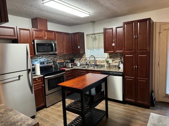 kitchen with tasteful backsplash, sink, stainless steel appliances, and light hardwood / wood-style flooring