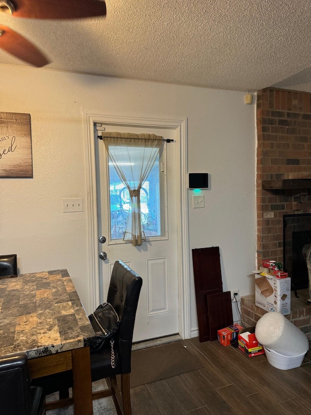 interior space featuring a textured ceiling, hardwood / wood-style flooring, a brick fireplace, and ceiling fan