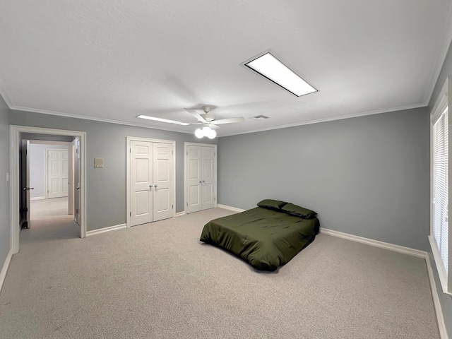 bedroom featuring ceiling fan, light carpet, two closets, and ornamental molding