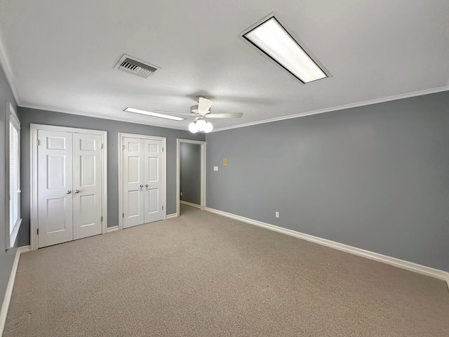 unfurnished bedroom featuring ceiling fan, ornamental molding, carpet floors, and two closets