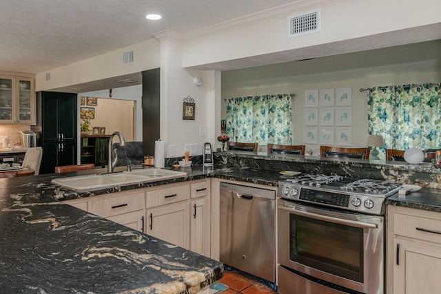 kitchen with a textured ceiling, a sink, visible vents, appliances with stainless steel finishes, and dark stone counters