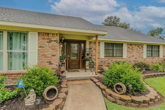 entrance to property featuring a shingled roof and brick siding