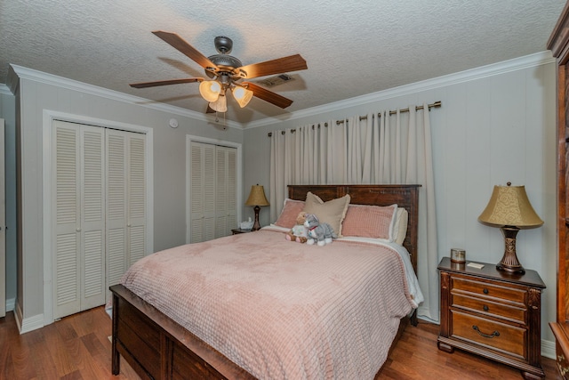 bedroom with a textured ceiling, ornamental molding, dark wood-type flooring, and two closets