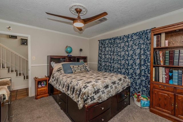 carpeted bedroom featuring crown molding, visible vents, a ceiling fan, wainscoting, and a textured ceiling