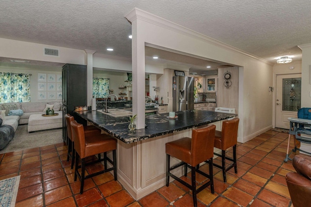 kitchen with stainless steel refrigerator with ice dispenser, visible vents, ornamental molding, a sink, and a kitchen breakfast bar