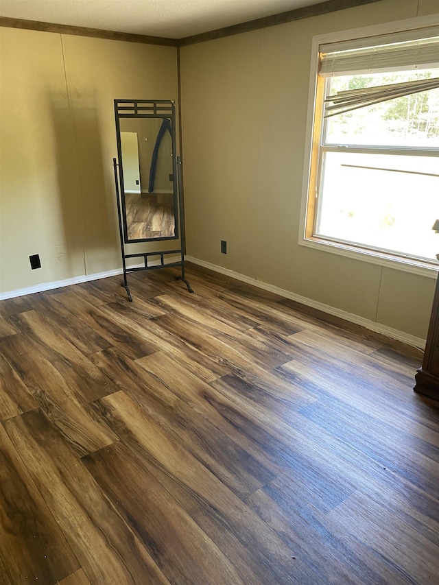 spare room with crown molding, dark wood finished floors, and baseboards