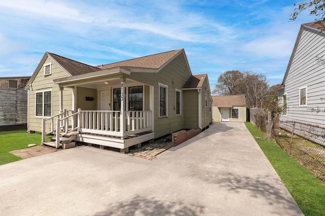 view of front facade with an outbuilding, fence, covered porch, a shingled roof, and a front lawn