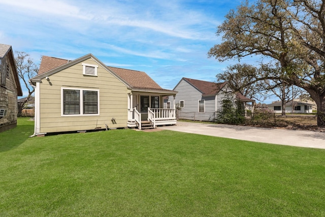 view of front facade featuring a front yard, a porch, driveway, and a shingled roof