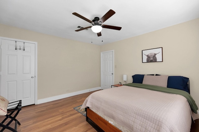 bedroom with ceiling fan, visible vents, baseboards, and wood finished floors