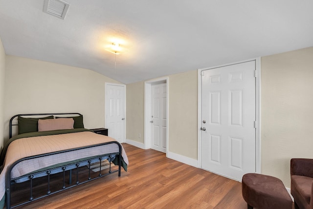 bedroom with visible vents, baseboards, lofted ceiling, and wood finished floors