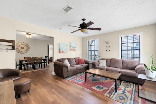 living room featuring a ceiling fan, wood finished floors, visible vents, and a healthy amount of sunlight