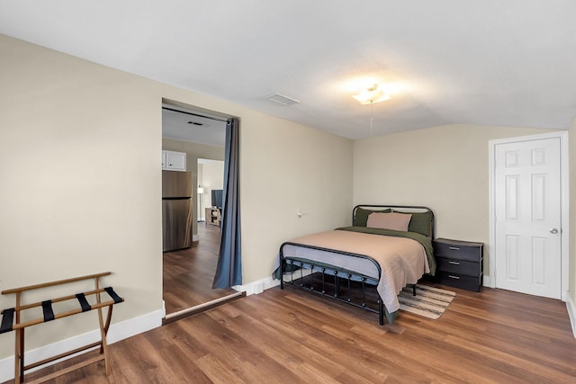 bedroom with wood finished floors, visible vents, baseboards, freestanding refrigerator, and vaulted ceiling