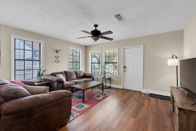 living room with visible vents, dark wood-type flooring, ceiling fan, and a textured ceiling