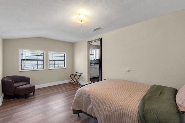 bedroom with wood finished floors, visible vents, baseboards, vaulted ceiling, and a textured ceiling