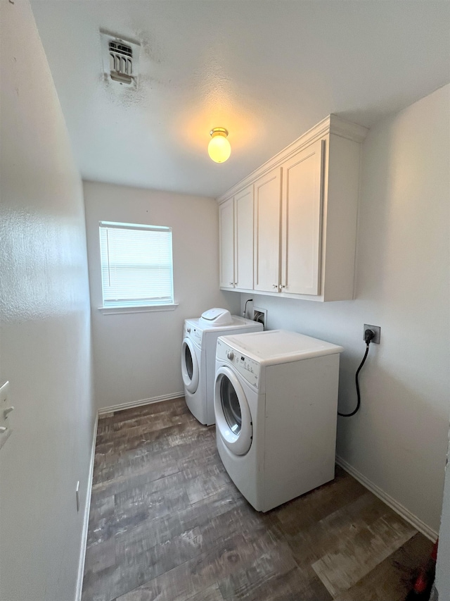 laundry area with dark wood-type flooring, washer and clothes dryer, and cabinets