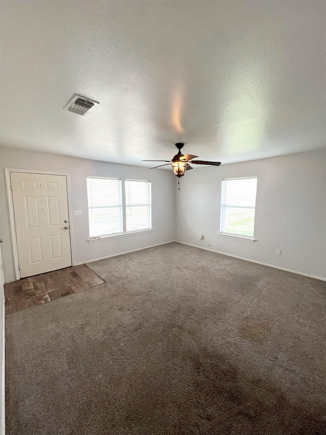 unfurnished living room featuring ceiling fan, dark carpet, and a textured ceiling