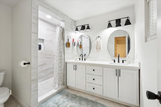 full bath featuring double vanity, toilet, marble finish floor, a tile shower, and a sink