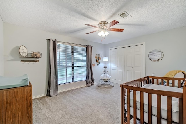 bedroom featuring a textured ceiling, ceiling fan, light colored carpet, and a crib