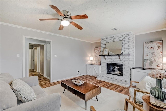 living room featuring a textured ceiling, light wood-type flooring, ornamental molding, ceiling fan, and a fireplace