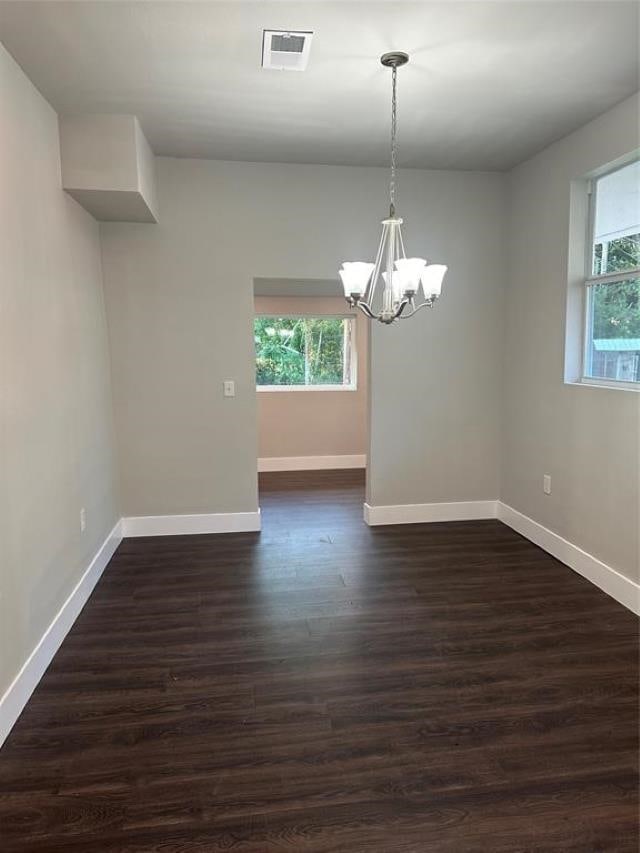 unfurnished room featuring a healthy amount of sunlight, dark hardwood / wood-style flooring, and a notable chandelier