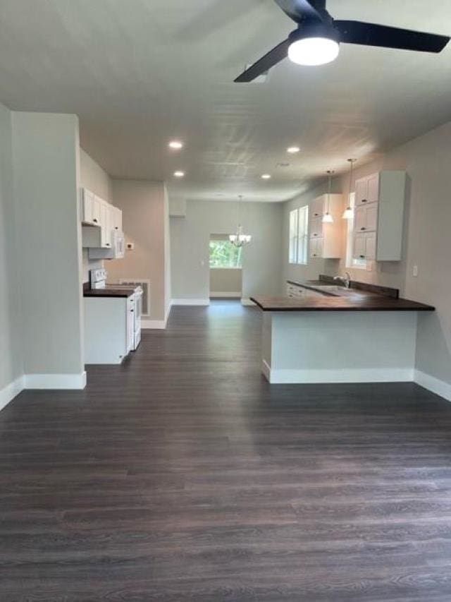 kitchen featuring white cabinetry, dark hardwood / wood-style floors, kitchen peninsula, pendant lighting, and ceiling fan with notable chandelier