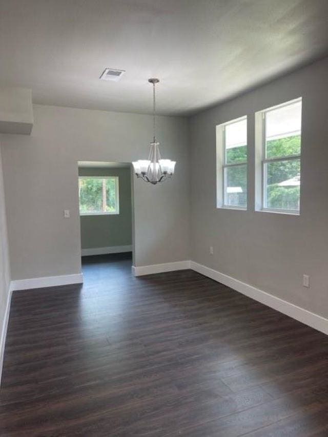 empty room featuring a notable chandelier and dark wood-type flooring