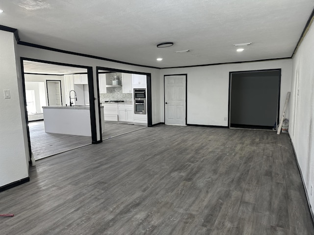 unfurnished living room featuring sink, ornamental molding, dark hardwood / wood-style floors, and a textured ceiling