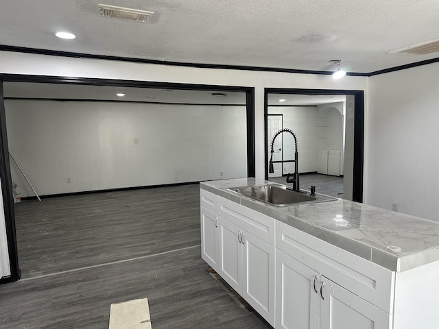 kitchen featuring dark hardwood / wood-style floors, sink, white cabinets, a center island with sink, and a textured ceiling