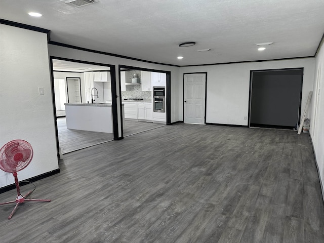 unfurnished living room featuring ornamental molding, dark hardwood / wood-style flooring, sink, and a textured ceiling