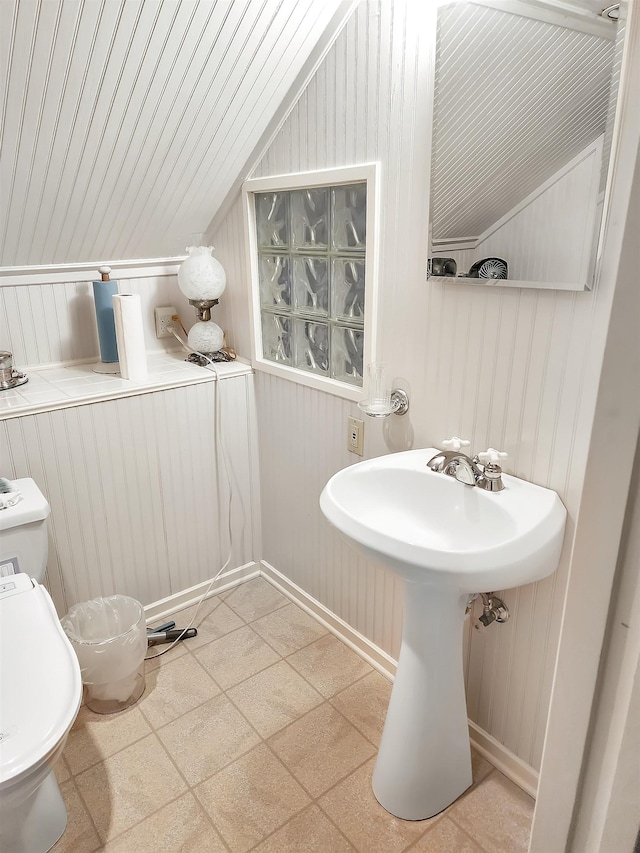 bathroom with lofted ceiling, toilet, and wooden walls