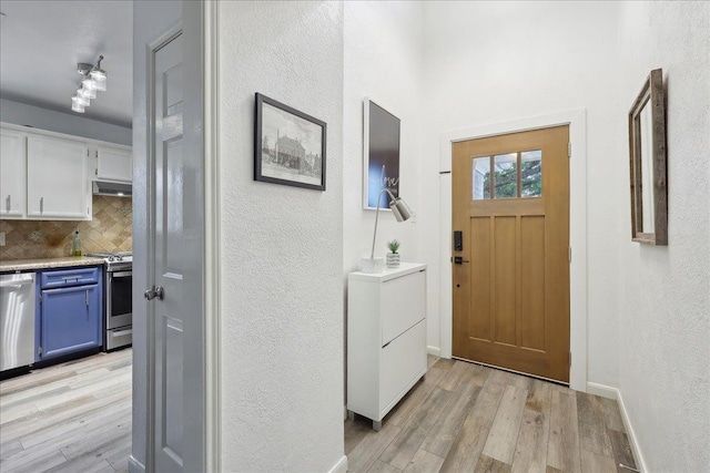 foyer entrance featuring baseboards, light wood-style flooring, and a textured wall