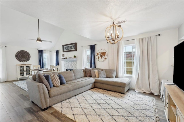 living area with ceiling fan with notable chandelier, vaulted ceiling, wood finished floors, and a textured ceiling