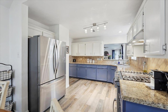 kitchen featuring blue cabinetry, a sink, white cabinets, appliances with stainless steel finishes, and wall chimney range hood