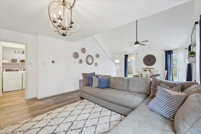 living area with light wood-style flooring, ceiling fan with notable chandelier, washing machine and dryer, baseboards, and vaulted ceiling