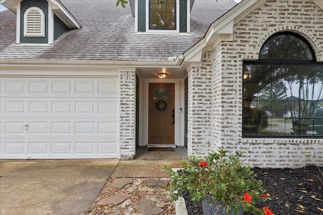 entrance to property with an attached garage, brick siding, roof with shingles, and driveway