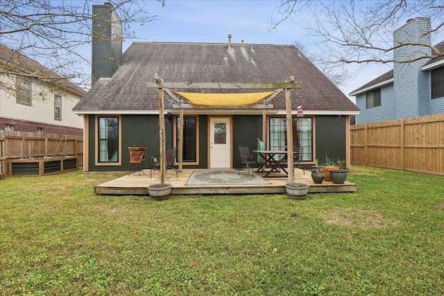 rear view of house featuring a deck, a lawn, roof with shingles, and a fenced backyard