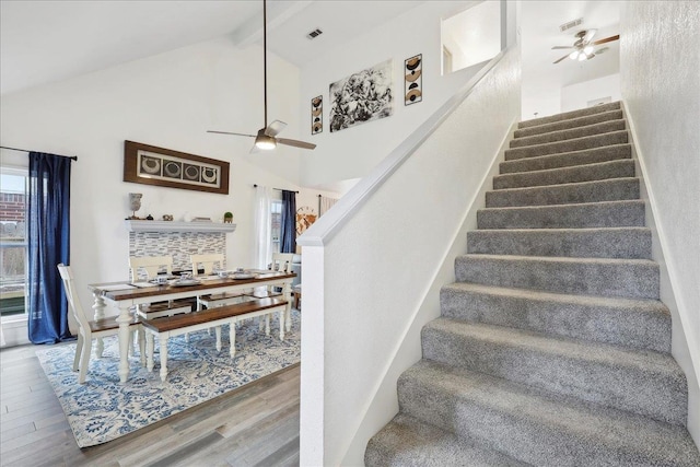 stairs featuring wood finished floors, beam ceiling, high vaulted ceiling, and ceiling fan