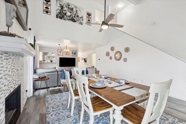 dining space featuring wood finished floors, a tiled fireplace, and ceiling fan with notable chandelier