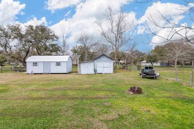 view of yard with a storage unit, an outbuilding, a fire pit, and fence