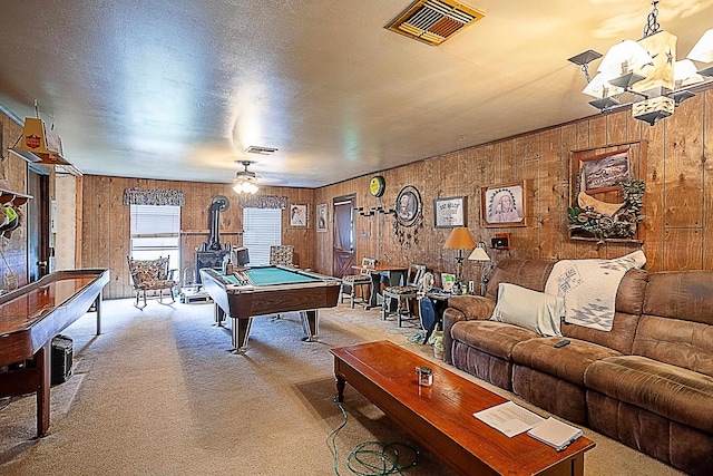 rec room with visible vents, a wood stove, a textured ceiling, light colored carpet, and a chandelier