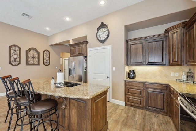 kitchen with stainless steel appliances, light wood-type flooring, light stone counters, an island with sink, and baseboards