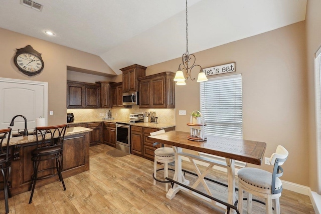 kitchen featuring stainless steel appliances, vaulted ceiling, decorative backsplash, light wood-type flooring, and decorative light fixtures