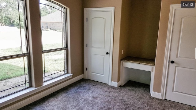unfurnished bedroom with dark colored carpet, multiple windows, and baseboards