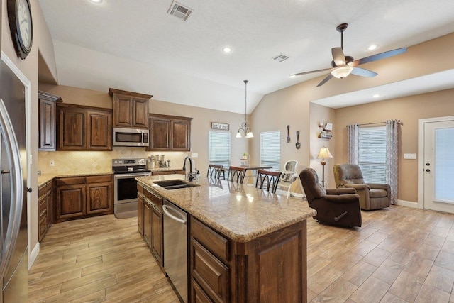 kitchen with appliances with stainless steel finishes, a sink, vaulted ceiling, light wood finished floors, and ceiling fan